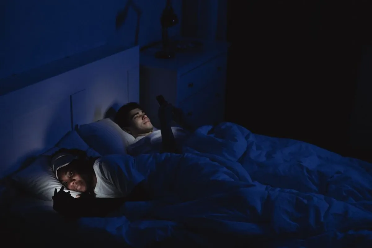Couple relaxed together at home in warm evening light, looking at their phones