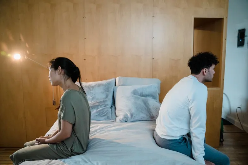 Couple lying apart in a quiet bedroom, distance between them in soft evening light