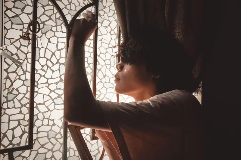 Person sitting alone by a window in soft, quiet light